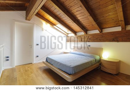 Cozy empty attic bedroom with wooden floor and ceiling with exposed beams