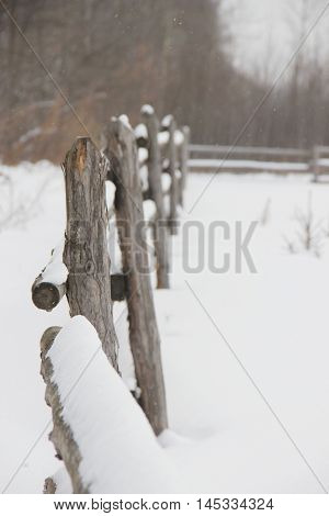 old rough rustic fence, made of logs, covered with snow