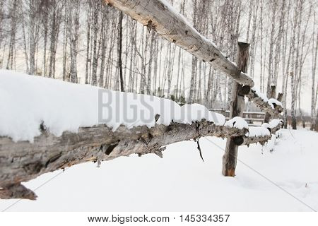 old rough rustic fence, made of logs, covered with snow