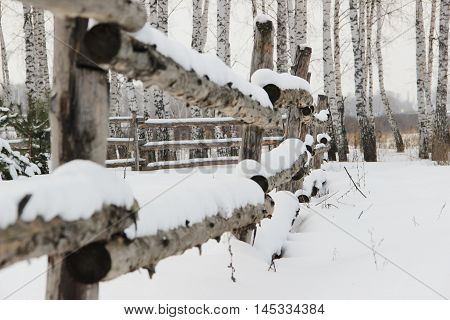 old rough rustic fence, made of logs, covered with snow