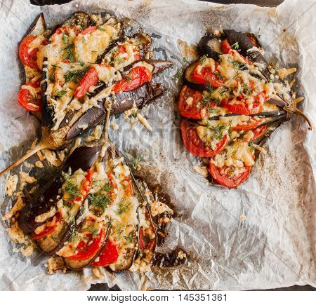 Baked eggplant in a fan shape on a baking sheet top view. Cooked with tomatoes and cheese. Sauce - olive oil garlic dried oregano and basil sprinkled with fresh dill.
