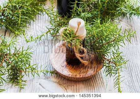 Juniper essential oil in a glass bottle on a wooden table. Used in medicine cosmetics and aromatherapy. Fresh green sprigs. Selective focus.