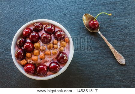 Breakfast bowl with yogurt granola or muesli or oat flakes fresh cherries and nuts. Black stone background top view.