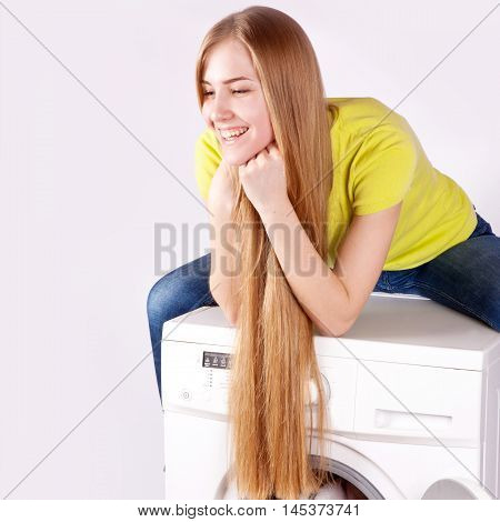 Beautiful happy girl with long blond hair sitting on the washing machine on a white background