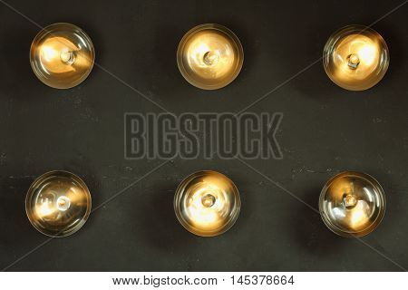 Six round lamps with lamp shades are on black wall in studio