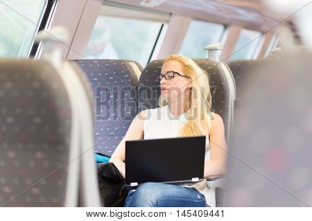 Businesswoman naping sitted while traveling by train and working on laptop. Tiresome business travel.