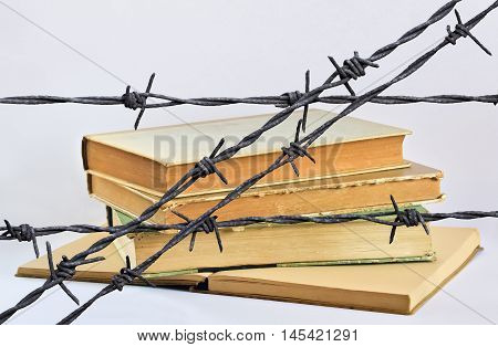 Stack of several old books behind a wire with barbs