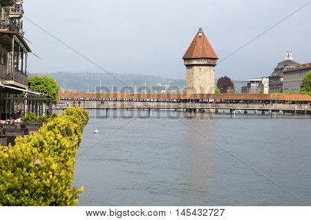 Lucerne Switzerland - May 02 2016: View towards the Chapel Bridge (Kapellbruecke) which joins two banks of the river Reuss together with the octagonal tall tower (Wasserturm) it is one of the Lucerne's most famous tourists attraction. A few people can be