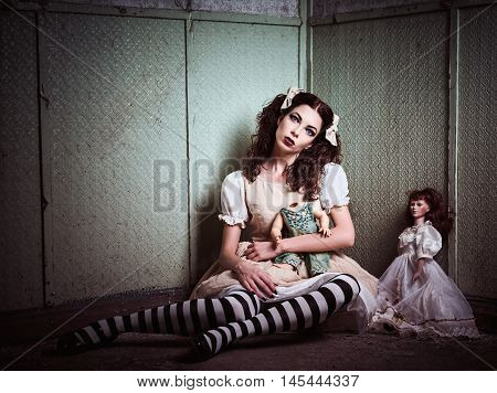 Strange sad girl with dolls sitting in the forsaken place
