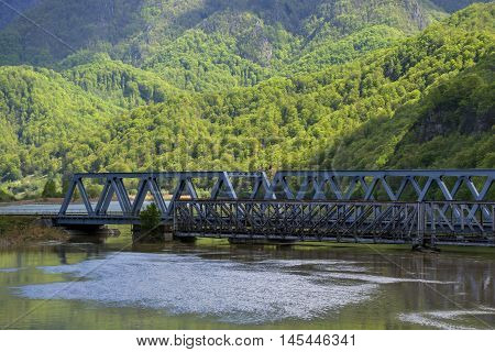 An old and new bridge crossing a big river with mountains in background