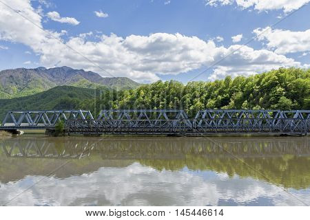 An old and new bridge crossing a big river with mountains in background