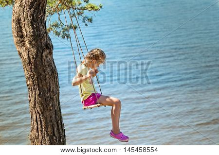little girl swinging on seesaw above a sea