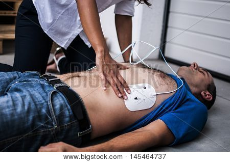 girl applying defibrillator electrodes to an unconscious man after heart attack