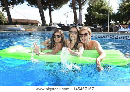 group of three happy and beautiful young girl friends having bath floating in airbed in swimming pool together having fun enjoying summer at vacation resort smiling in women holiday concept