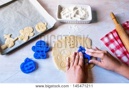Making cookies for Halloween and Thanksgiving. Fun food for kids, a snack for a party. Woman cut out cookies using cookie cutters, hands in the frame