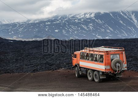 KAMCHATKA PENINSULA RUSSIA - JUNE 24 2016: Russian expedition truck KamAZ (6-wheel drive) on mountain road on background of lava fields and volcanoes. Eurasia Russian Far East Kamchatka Region Klyuchevskaya Group of Volcanoes.