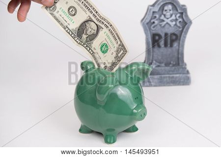 American dollar going into a green piggy bank with tombstone in background, white background