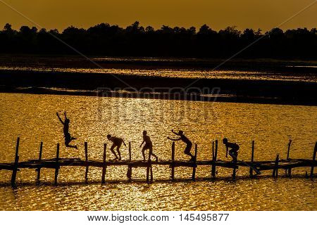 Children on wooden old bridge are jumping into the river in rural of Thailand