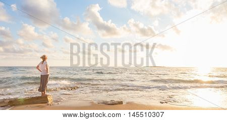 Relaxed woman enjoying sun, freedom and life an beautiful beach in sunset. Young lady feeling free, relaxed and happy. Concept of vacations, freedom, happiness, enjoyment and well being.