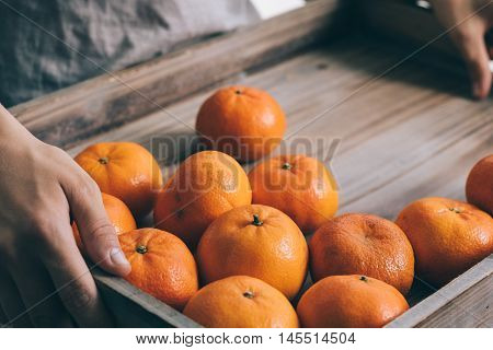 Hand holding a wooden tray with tangerines
