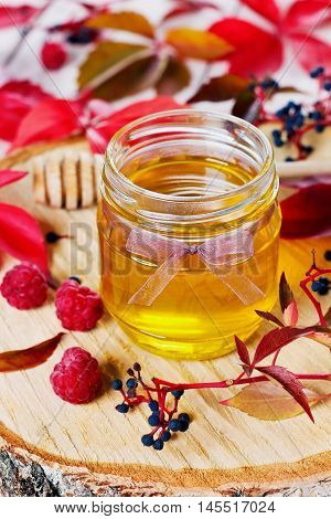 Sweet honey in pot with bow on a wooden background decorated autumn leaves and raspberry, focus on the front of the pot.