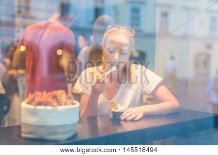 Young pretty woman eating icecream in gelateria. Through the window view.