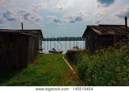 Lake view with old wooden barns small pier and boats in summer.