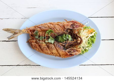 Fried Seriola fish in blue dish on wooden background.