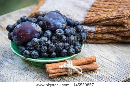 Aronia melanocarpa (Black chokeberry) and plums on wooden table. Home atmosphere. Autumn concept. Autumn harvest. Knitted things