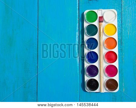 The palette of watercolor paints on a blue wooden background. Copy space