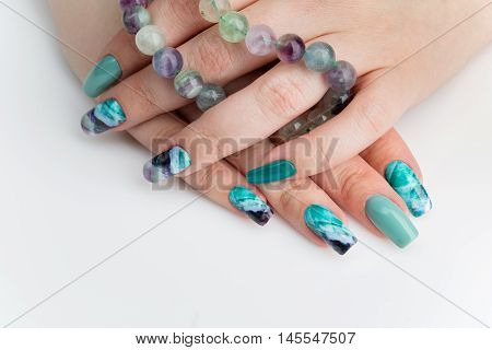 Closeup of woman nails with creative purple and green manicure. Fluorinit print. Natural stone beads. Copy space.