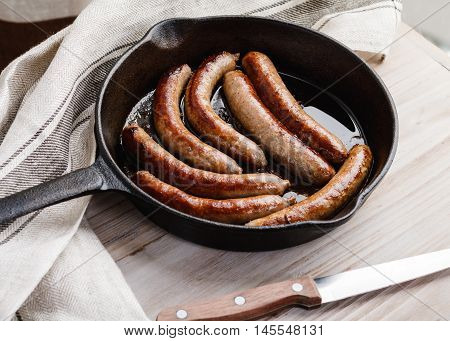 Fried sausage in a cast iron frying pan on a wooden table