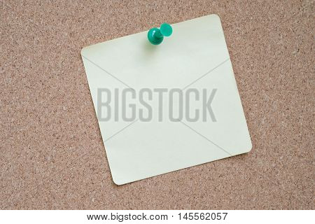 Yellow sticker pinned green pushpin with cork background.