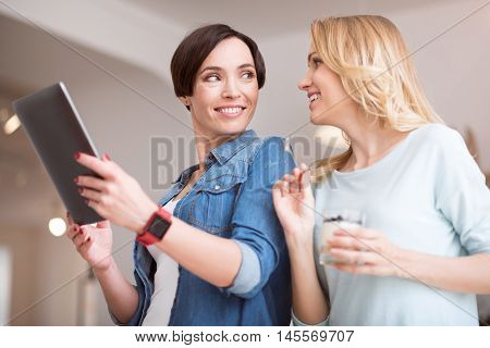 Our communication. Delighted and smiling women eating sweet deserts and using digital tablet while relaxing together