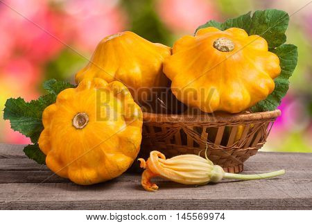 yellow pattypan squash with leaf in a wicker basket on a wooden table with a blurred background.