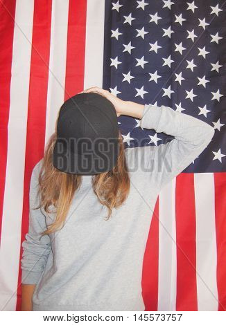 Lifestyle portrait of young teenage girl standing against  isolated american flag background dressed in casual clothes gray sweater and black snapback cap with hair down