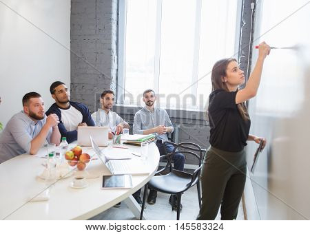 Business or freelance workshop session. Young businesswoman writing new business plan or stategy for companies, enterprises or firms while performing in board room in office.