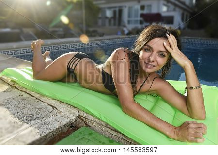 young sexy woman in bikini with fit beautiful body having suntan relaxing on airbed at swimming pool of vacation hotel resort in summer enjoying holidays with sun lens flare on sunset