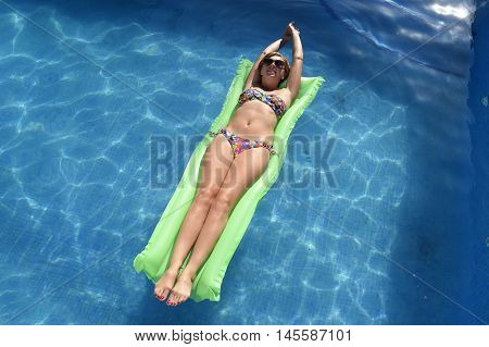 young happy beautiful woman in bikini and sunglasses lying relax on float airbed at vacation hotel resort swimming pool in Summer enjoying holidays having sunbath with tan body
