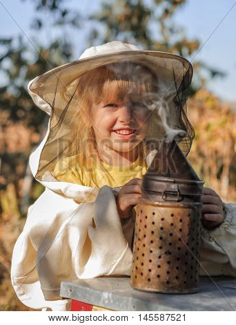 Little girl beekeeper blows smoker for bees.