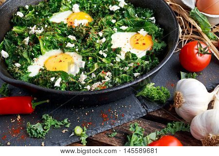 Homemade Green Kale with eggs, feta cheese, herbs in iron pan. healthy rustic breakfast.