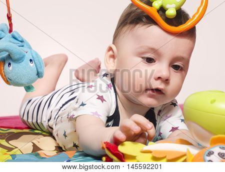 Cute baby boy sitting on a playmat and playing with toys. Adorable six month old child happy crawling to reach the toys.