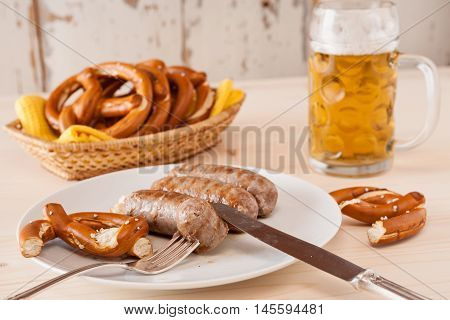 Bavarian cooked sausage and pretzel on a breadbasket and beer on background