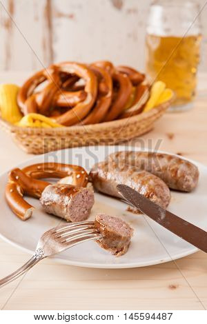 Closeup of bavarian cooked sausage and pretzel on a breadbasket and beer on background
