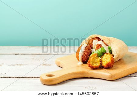Falafel balls in pita with tahini sauce on wooden board