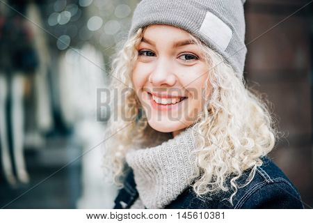 Portrait of young beautiful blond curly smiling girl in warm clothes in the street