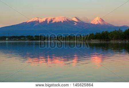 Sunset lighting Kluchevskaya group of volcanoes with reflection in the river Kamchatka.