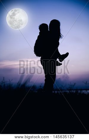 Silhouette of mother and child enjoying friendly family. Mother giving children piggyback. Happy family spending time together. Cool colors tone photo effect. The moon were NOT furnished by NASA.