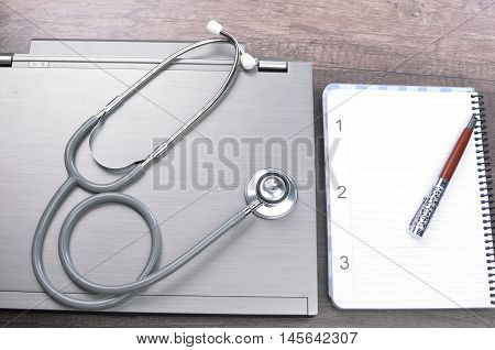 Grey stethscope on top of laptop at wooden background