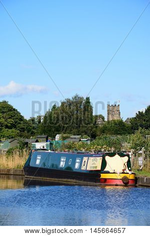 ARMITAGE, UNITED KINGDOM - AUGUST 8, 2016 - Narrowboat moored on the canal with allotments and church to the rear Armitage Staffordshire England UK Western Europe, August 8, 2016.